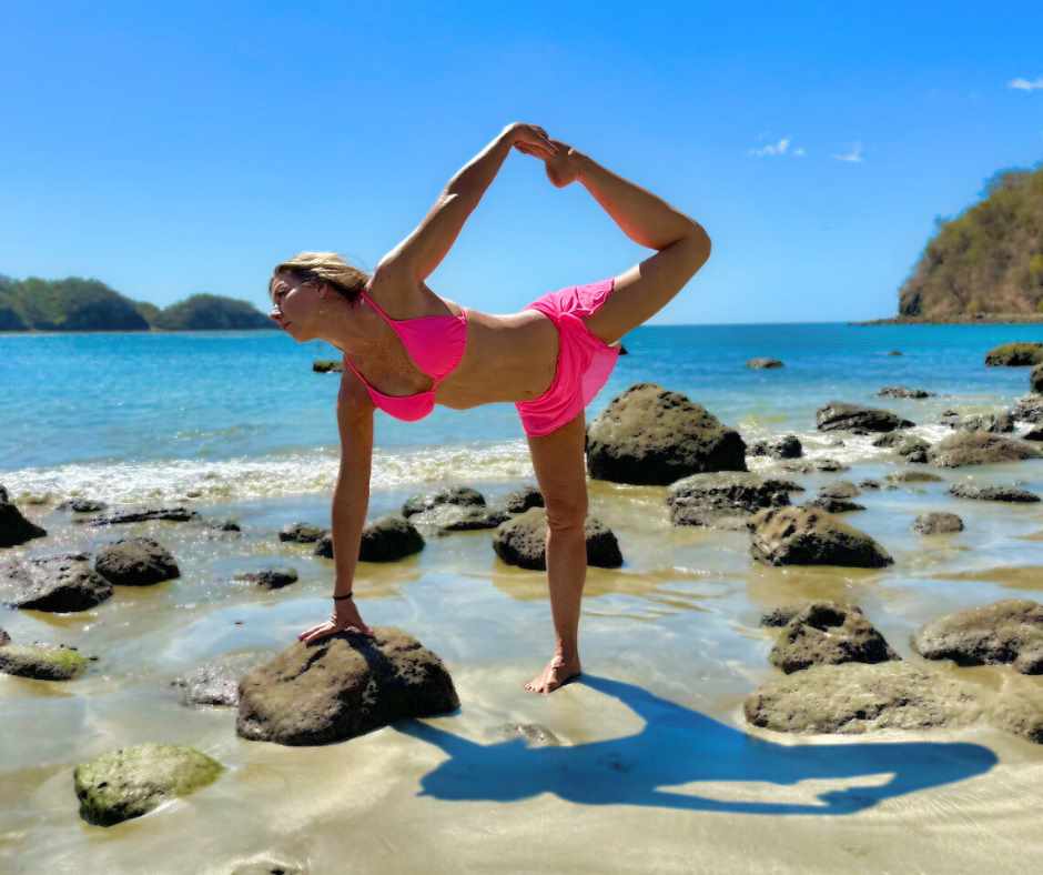 A woman in pink bikini doing yoga on the beach.